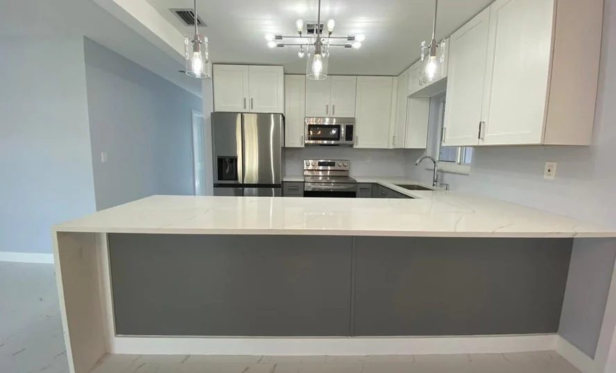 Completed modern kitchen featuring a large light countertop island, white cabinets and clean gray finishes